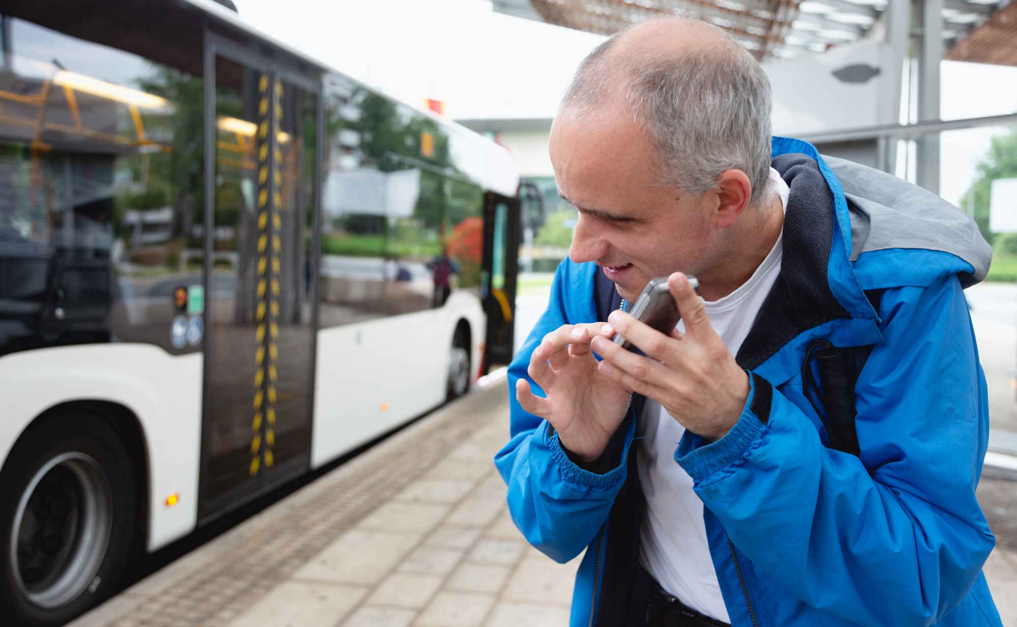 Image d'illustration représentant une personne aveugle consultant des informations sur son téléphone, à un arrêt de bus