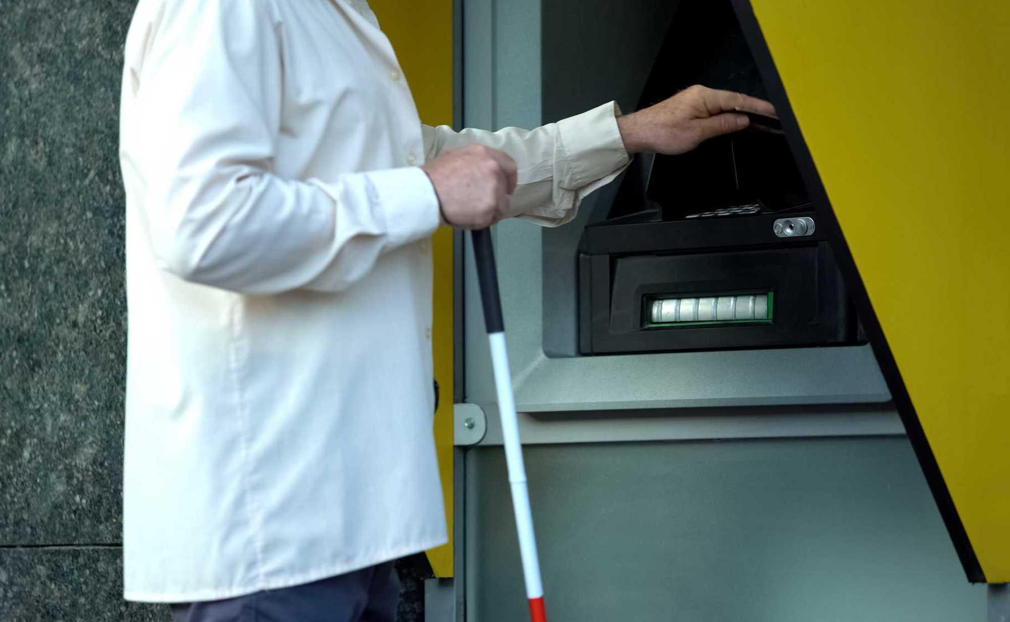 Photo d'illustration montrant un homme en train de retirer de l'argent d'un guichet équipé d'indicateurs tactiles