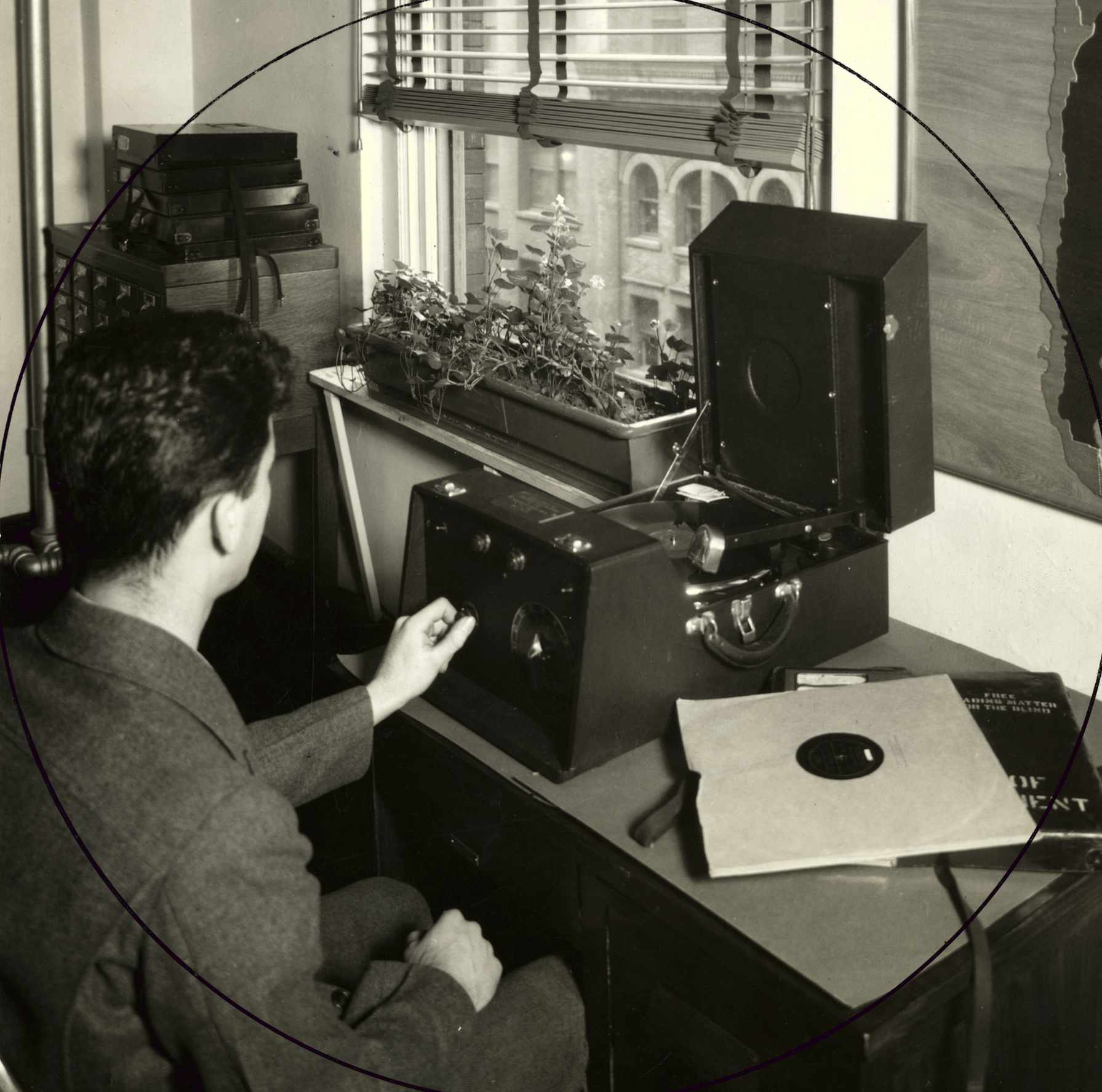Un homme assis devant un bureau utilise un dispositif ressemblant à un volumineux tourne-disque portatif